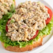 Vegan tuna on a slice of bread, with lettuce and tomato slices, on a white plate.