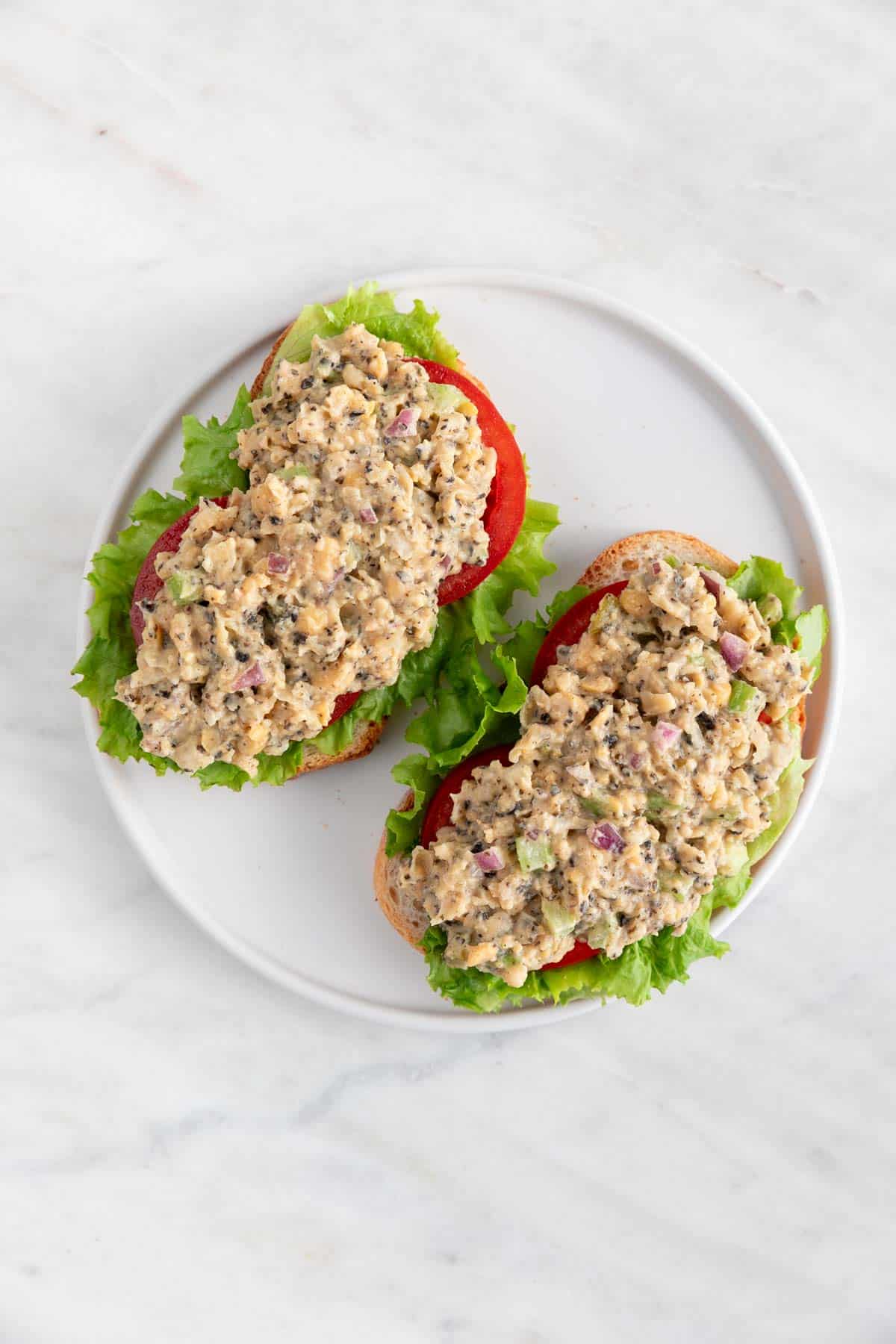 Two slices of bread with vegan tuna, lettuce, and tomato slices.