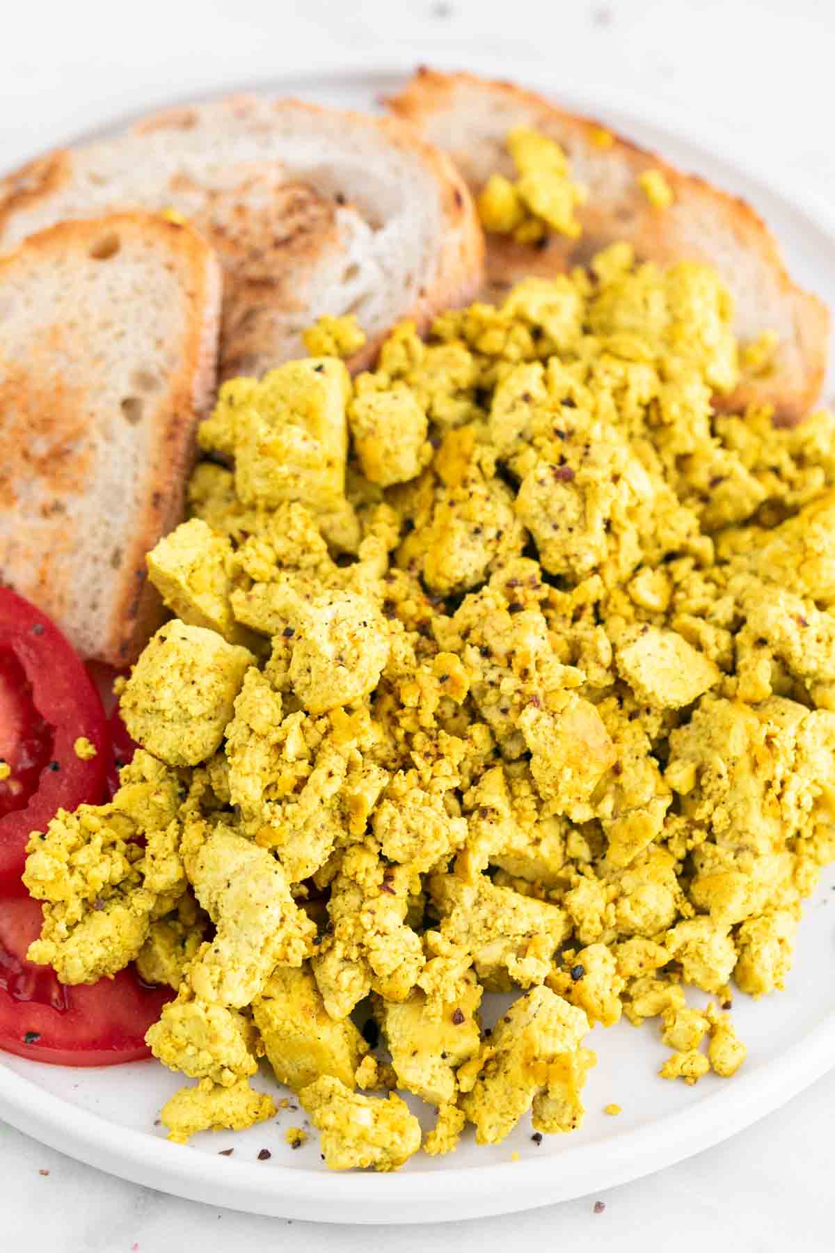 Scrambled tofu with bread and tomato on a plate.