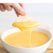 Hand dipping a tortilla chip into vegan cheese dip.