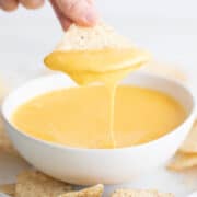 Bowl of vegan cheese with a hand dipping a tortilla chip.