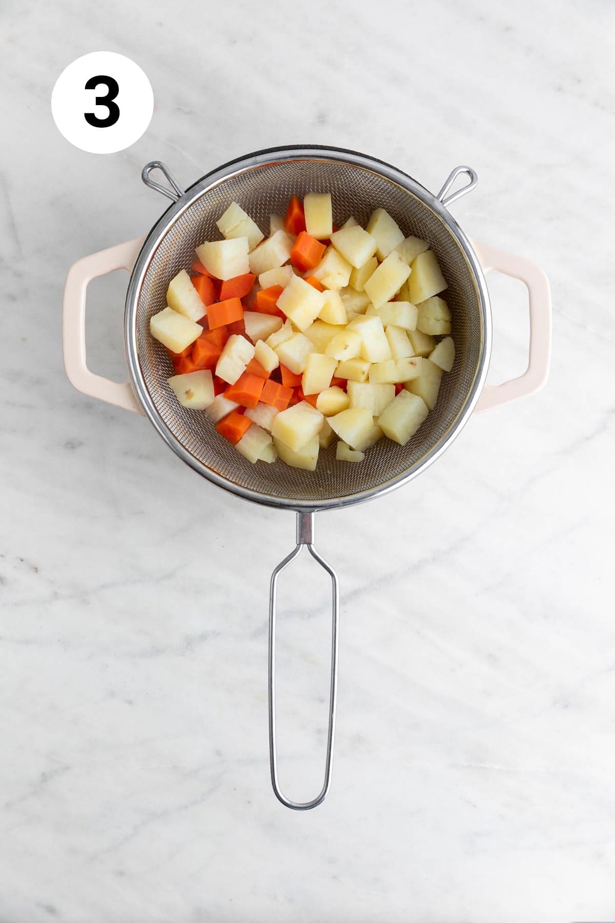 Boiled potatoes and carrots draining in a colander over a pot.