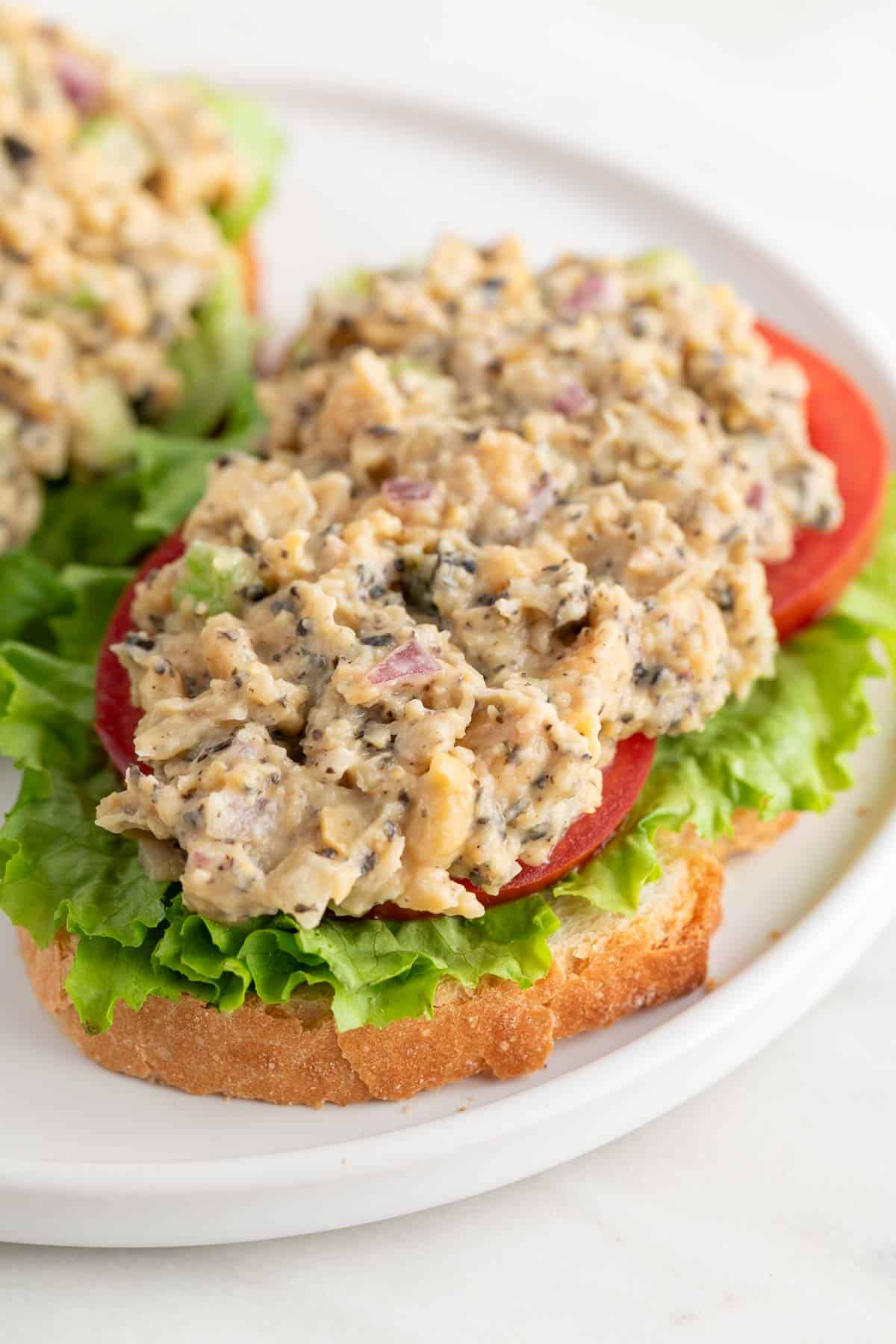 Vegan tuna on a slice of bread with lettuce and tomato slices.