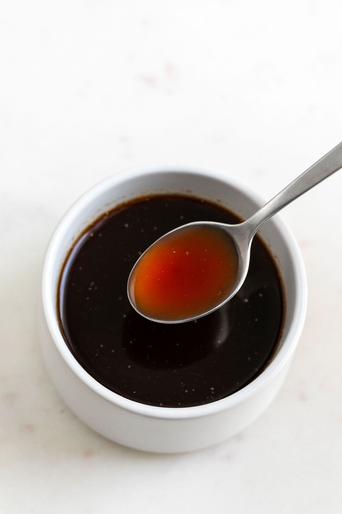 Spoon dipping into vegan Worcestershire sauce bowl.