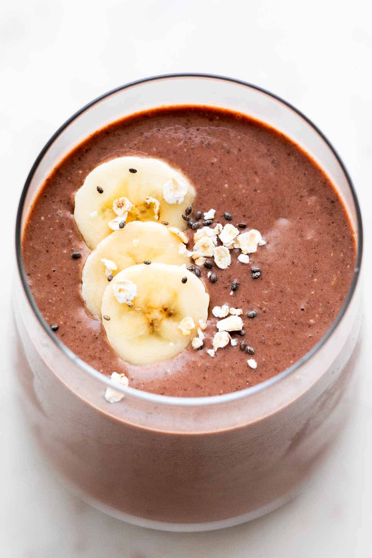 Glass of vegan protein shake garnished with banana, oats, and chia seeds.