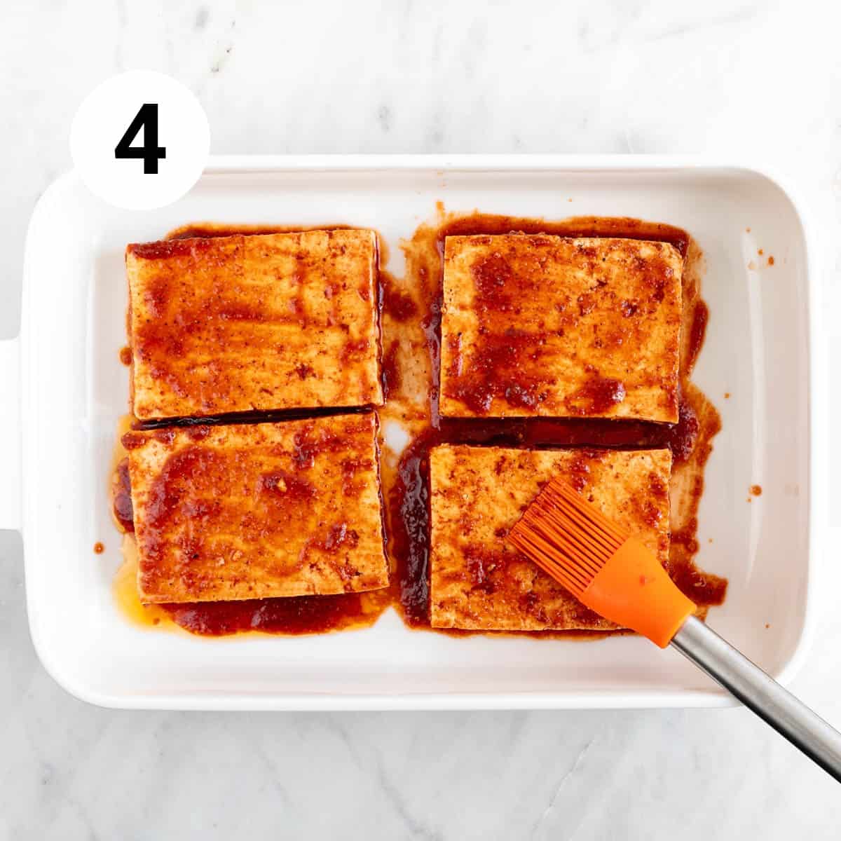 Four tofu steaks in a baking dish being brushed with marinade.