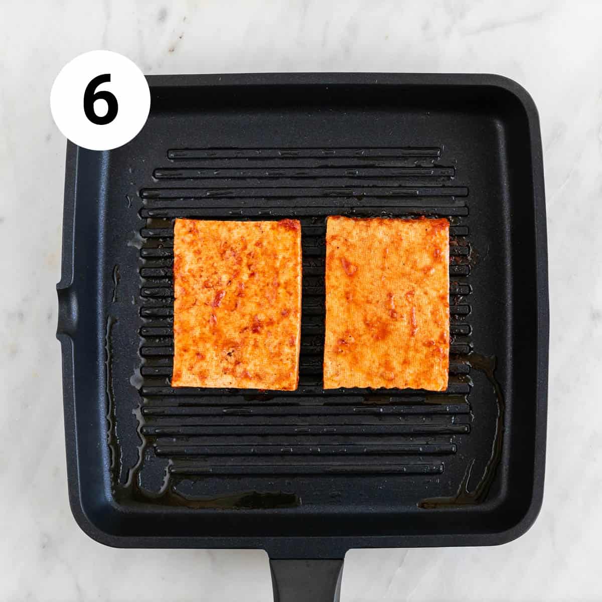 Two tofu steaks cooking in a grill pan.