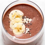 Vegan protein shake in glass topped with banana, oats, and chia seeds.