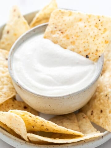 Vegan sour cream surrounded by tortilla chips with one chip dipped inside.