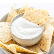 Bowl of vegan sour cream with a tortilla chip dipped in.