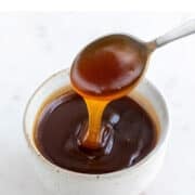 Spoon dipping into bowl of vegan caramel sauce.