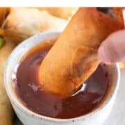 A vegan spring roll dipping into a bowl of sweet and sour sauce.