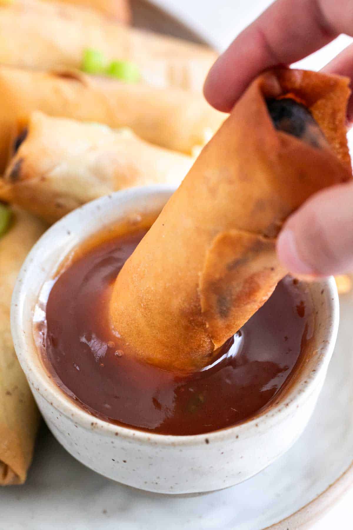 A vegan spring roll dipping into a bowl of sweet and sour sauce.