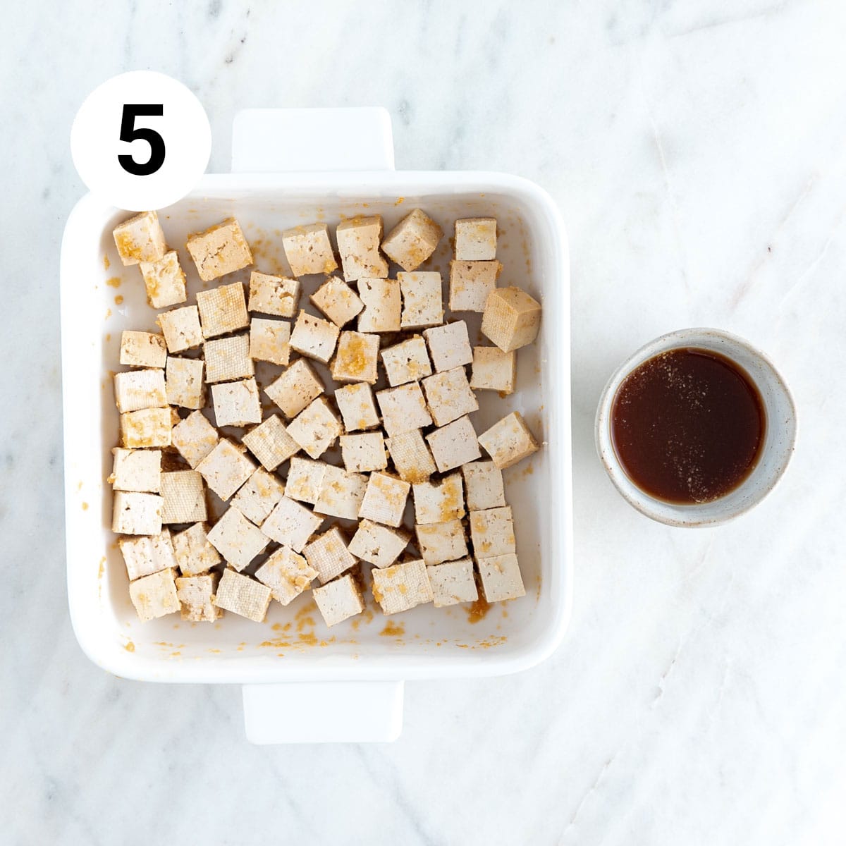 Tofu cubes in a baking dish and marinade in a bowl.