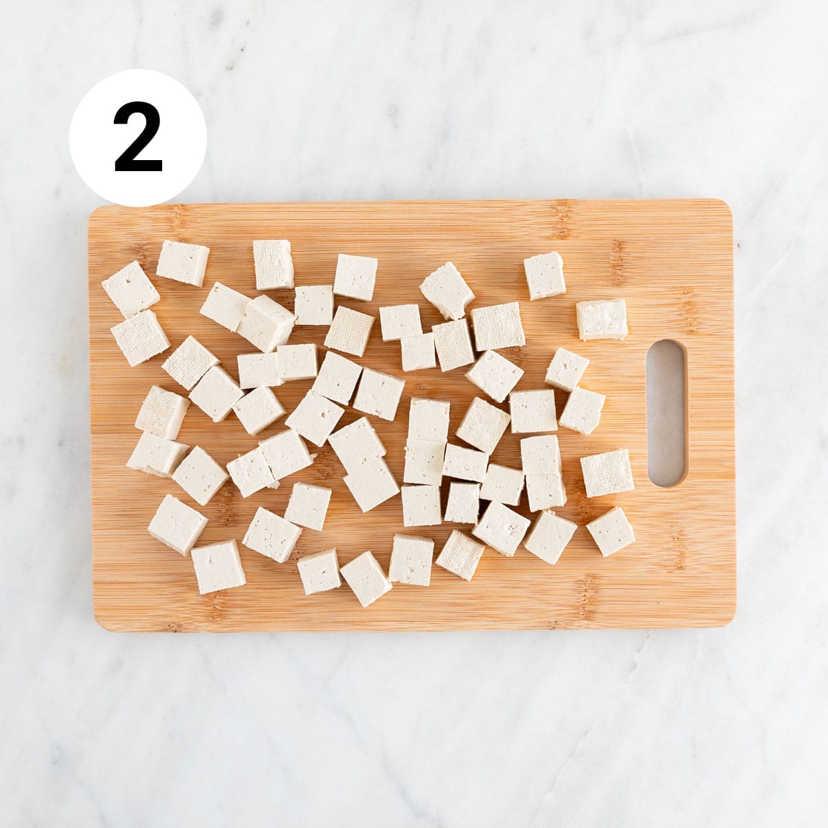 Tofu cubes on wooden cutting board.
