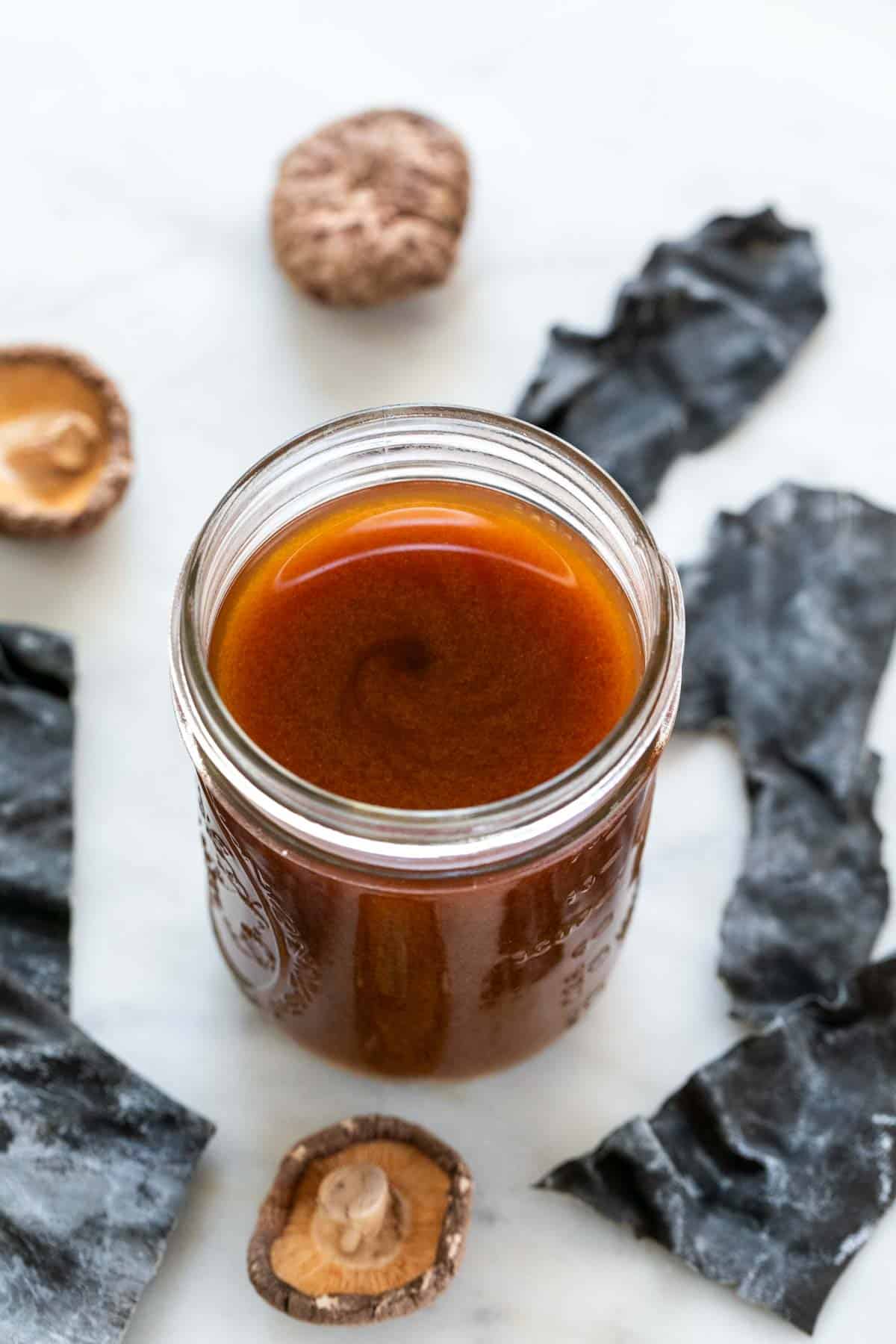 Vegan fish sauce in a jar with seaweed and dried mushrooms in the background.