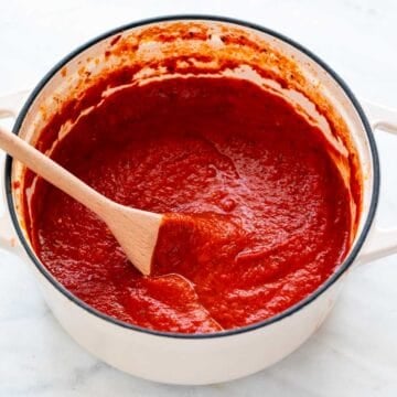 Homemade marinara sauce in a large pot stirring with a spoon.
