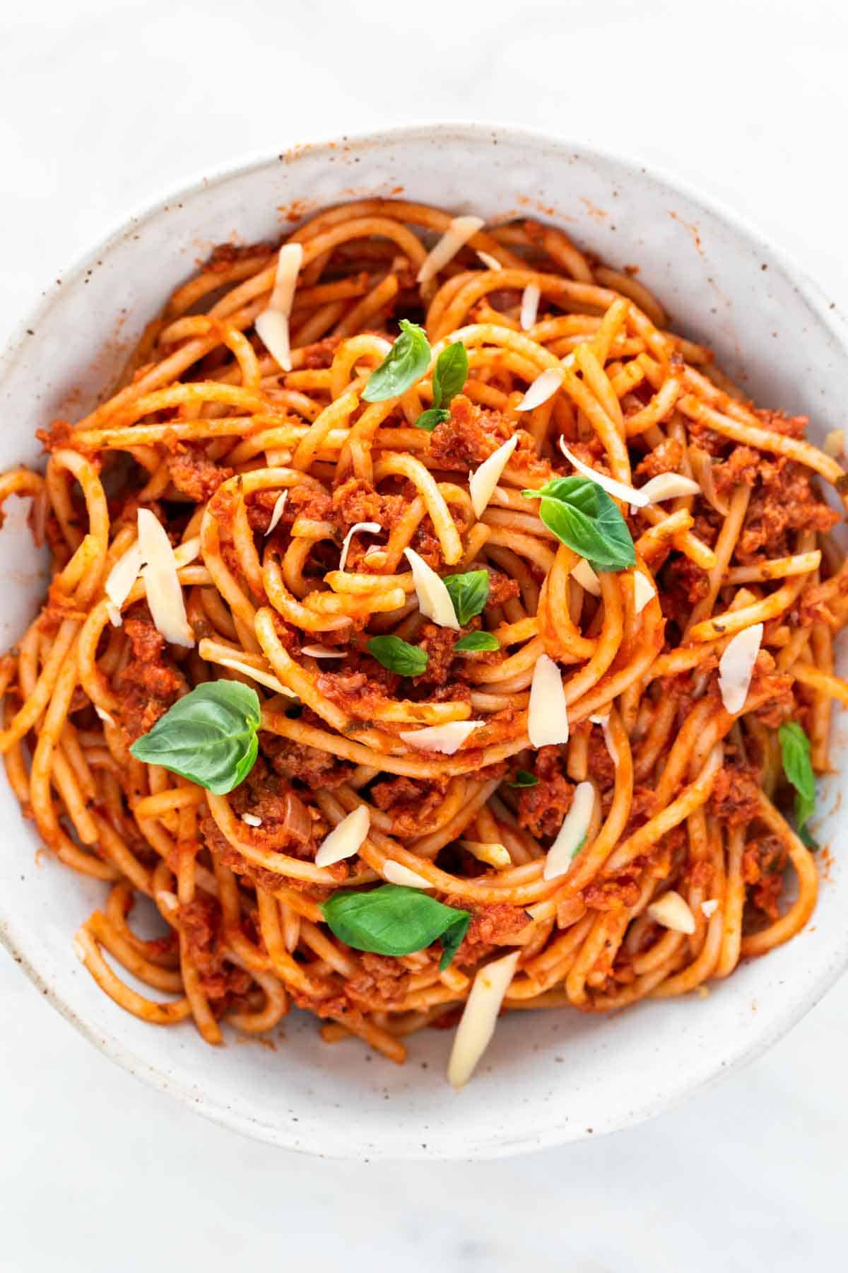 A bowl of vegan spaghetti with vegan cheese and basil on top.