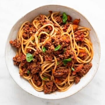Vegan bolognese pasta in a bowl garnished with basil.