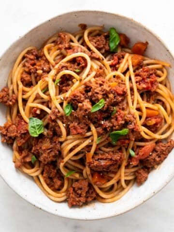 Vegan bolognese pasta in a bowl garnished with basil.