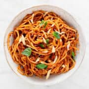 Vegan spaghetti in a bowl with basil leaves and shredded vegan cheese on top.