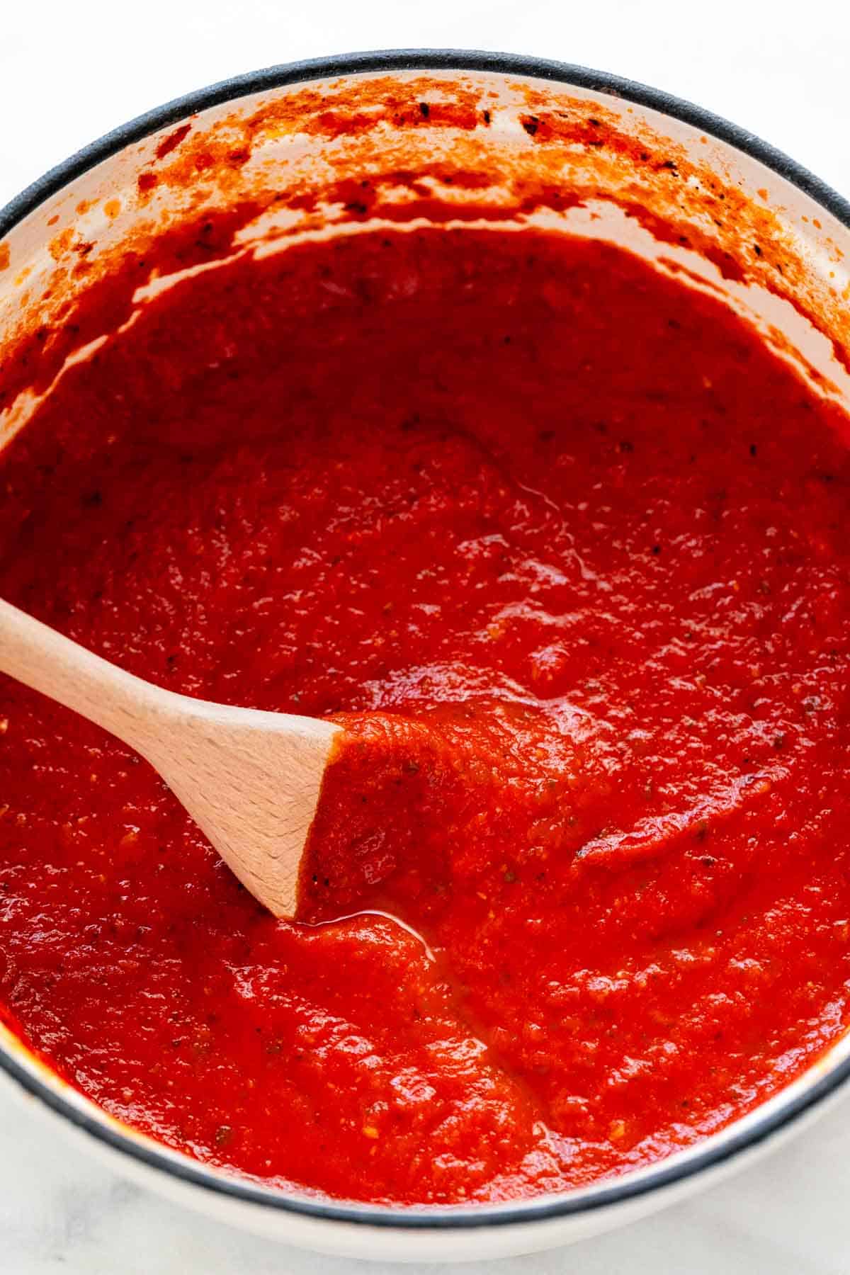 Homemade marinara sauce in a large pot with a wooden spoon.