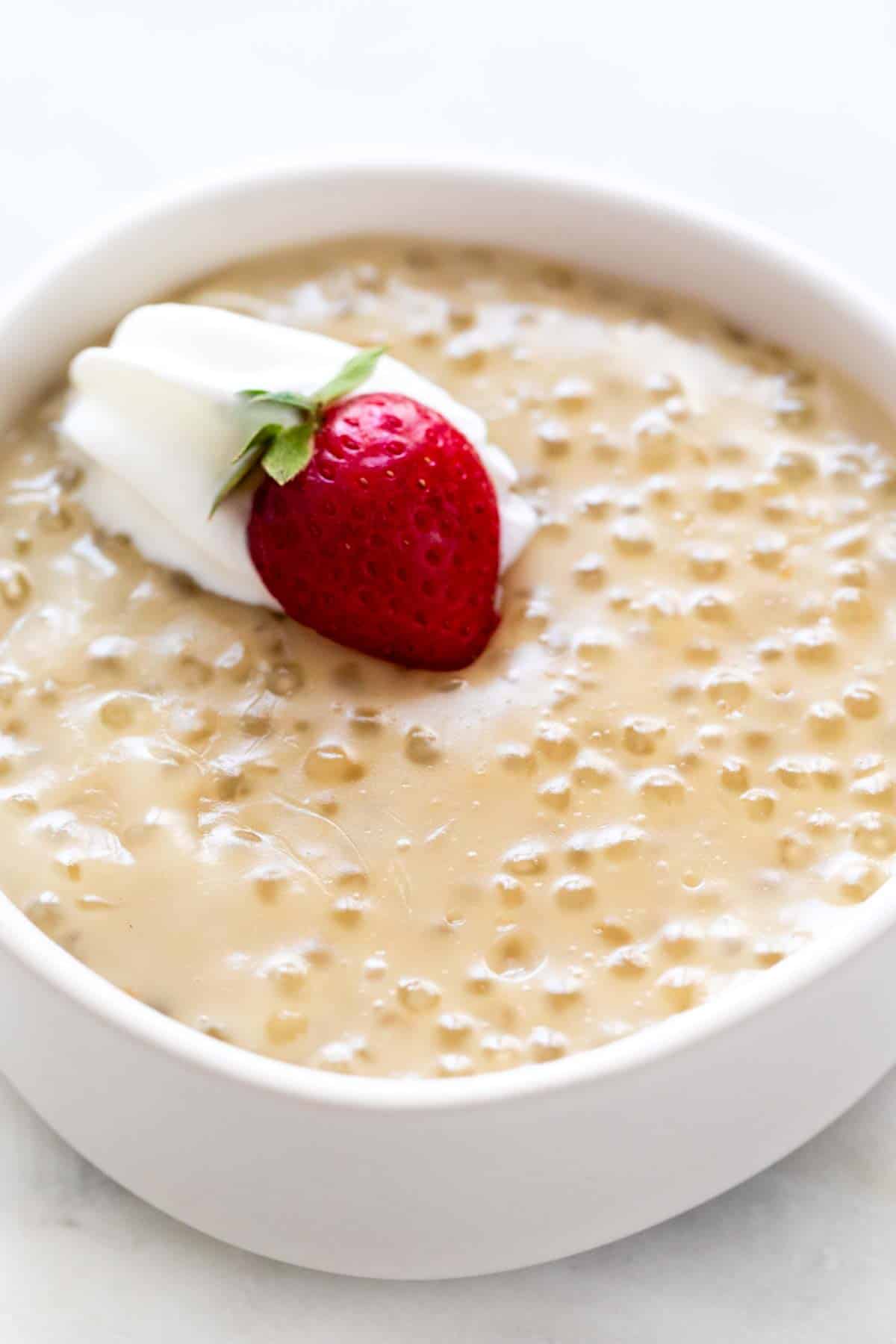 Vegan tapioca pudding in bowl garnished with vegan whipped cream and a strawberry.