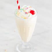 Vegan ice cream in a glass topped with various toppings and a straw.