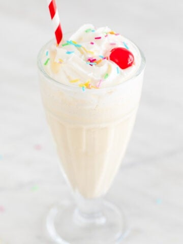 Vegan ice cream in a glass topped with various toppings and a straw.