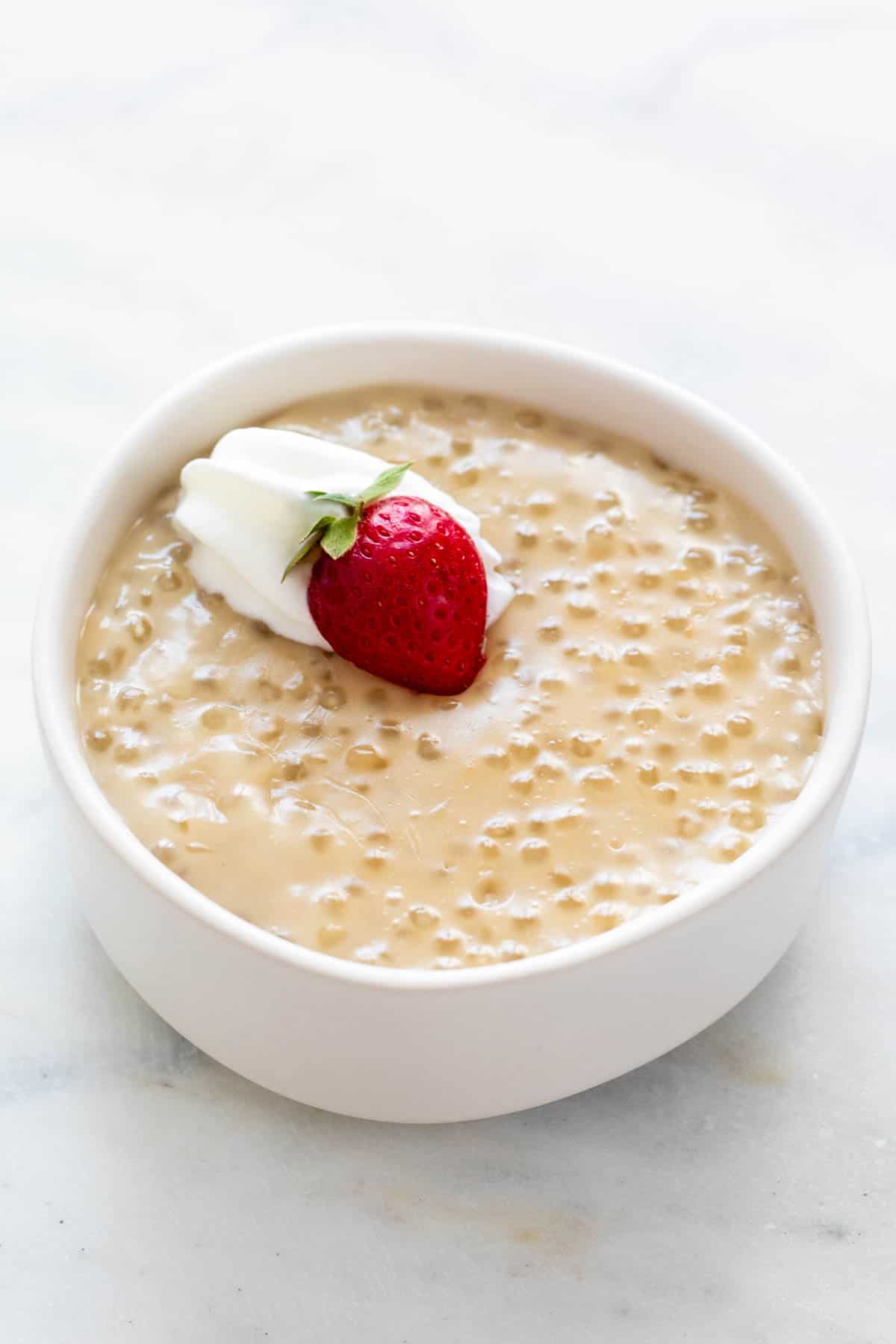 Bowl of vegan tapioca pudding topped with vegan whipped cream and a strawberry.