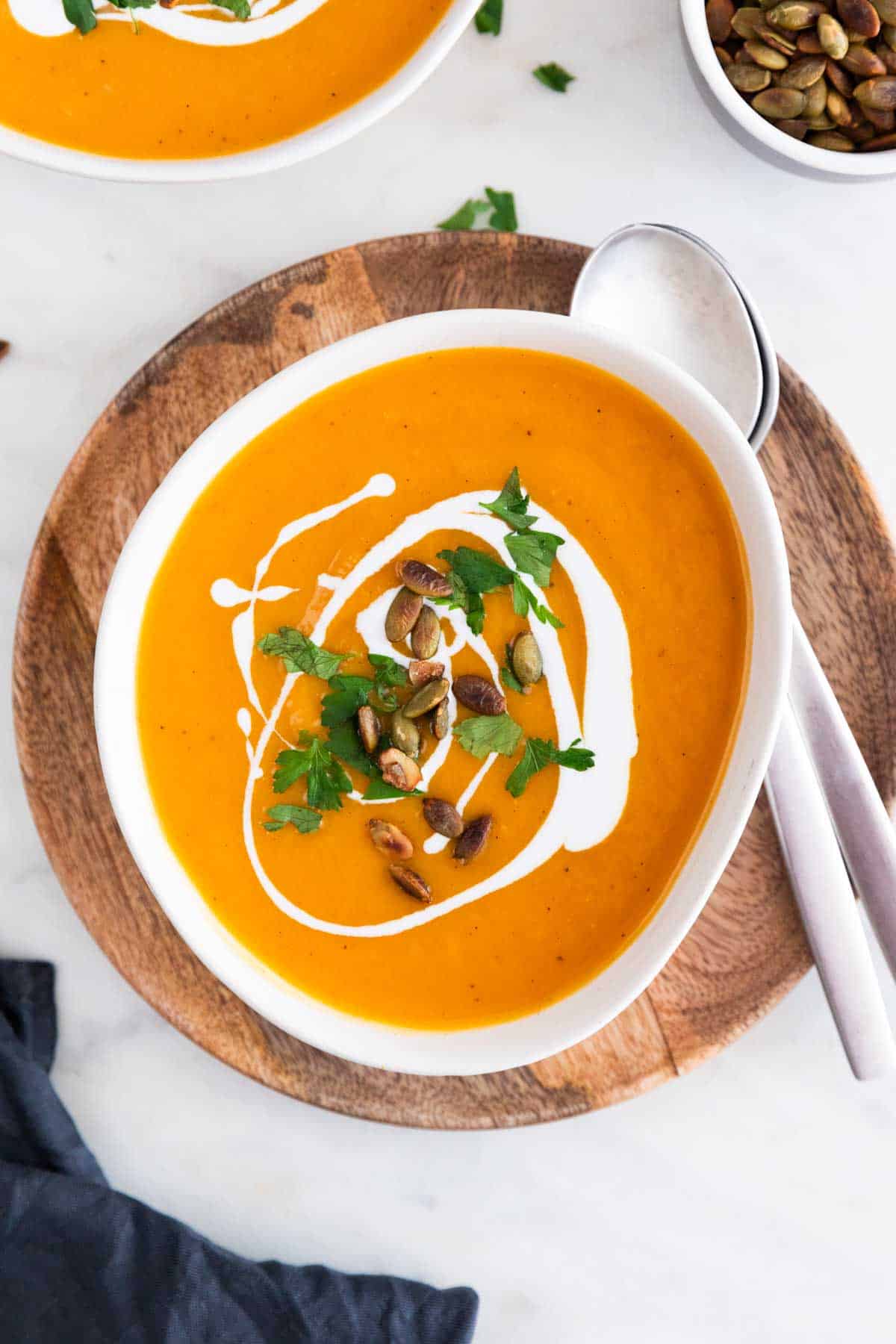 Vegan butternut squash soup in a bowl with parsley, coconut milk, and pumpkin seeds.