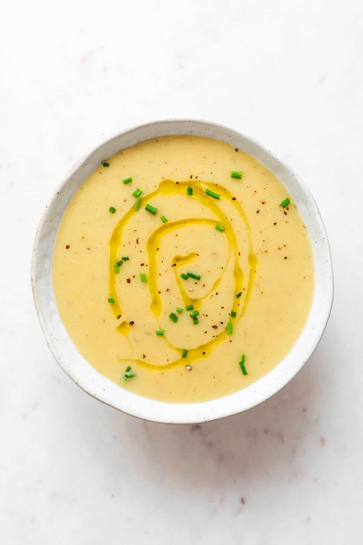 Bowl with vegan potato soup garnished with olive oil, pepper, and chives.