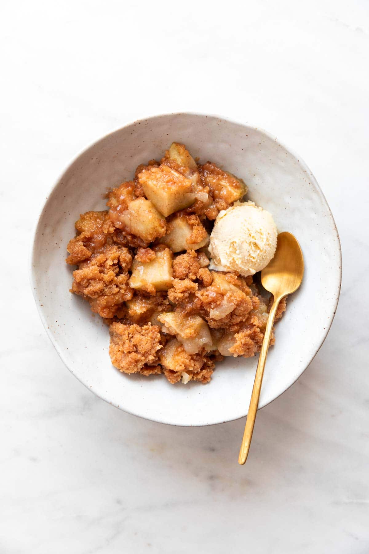 Vegan apple crumble in a bowl with a scoop of ice cream and a spoon.