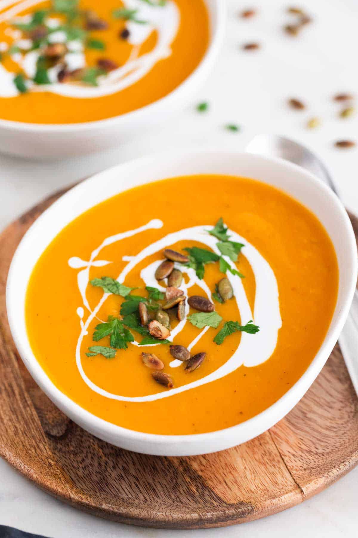 Bowl of vegan butternut squash soup garnished with another bowl in the background.