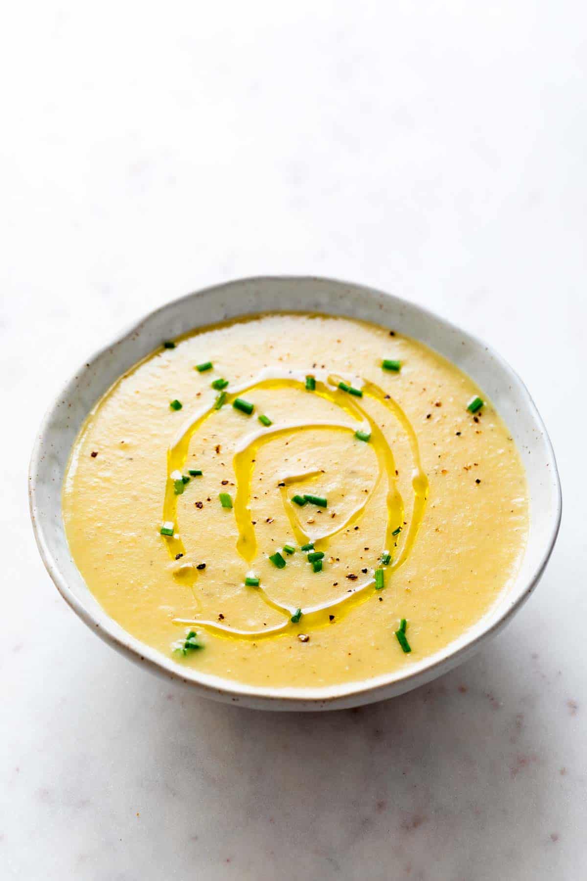 Vegan potato leek soup in a bowl topped with olive oil, black pepper, and chives.