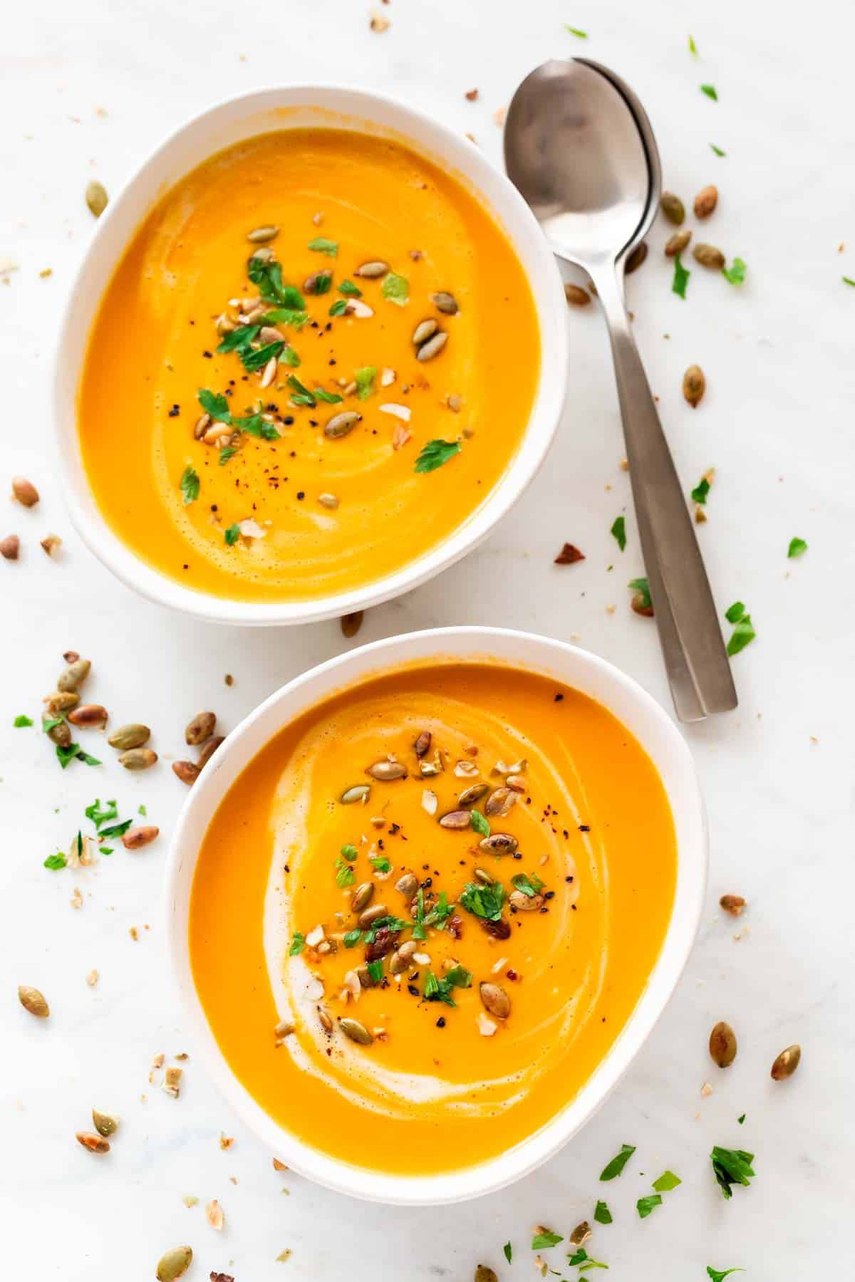 Two bowls of vegan pumpkin soup, each garnished with coconut milk, parsley, and black pepper.