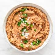 Vegan refried beans served in a bowl, topped with fresh onion and parsley.