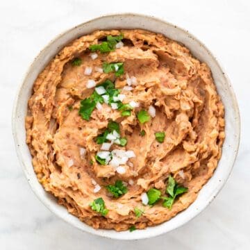 Vegan refried beans served in a bowl, topped with fresh onion and parsley.