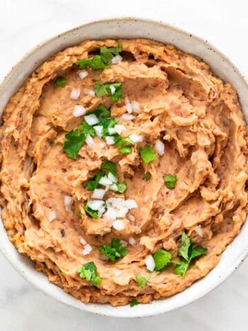 Vegan refried beans served in a bowl, topped with fresh onion and parsley.