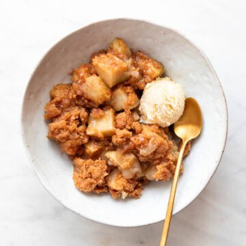 Bowl of vegan apple crumble served with ice cream and a spoon on the side.