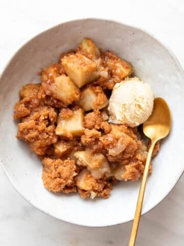 Bowl of vegan apple crumble served with ice cream and a spoon on the side.