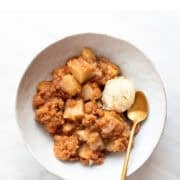 Vegan apple crumble in a bowl with a scoop of ice cream and a spoon.