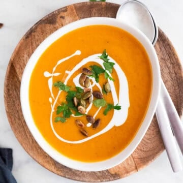 Vegan butternut squash soup bowl garnished with parsley, coconut milk, and pumpkin seeds.