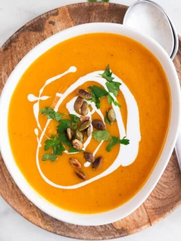 Vegan butternut squash soup bowl garnished with parsley, coconut milk, and pumpkin seeds.