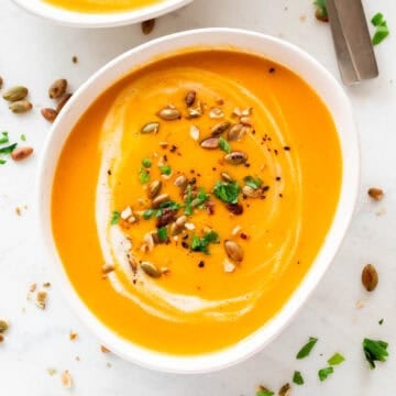 Bowls of vegan pumpkin soup, topped with coconut milk, parsley, and a dash of black pepper.