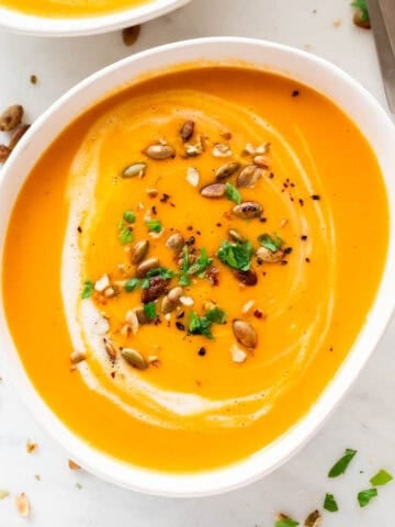 Bowls of vegan pumpkin soup, topped with coconut milk, parsley, and a dash of black pepper.