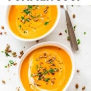 Two bowls of vegan pumpkin soup, each garnished with coconut milk, parsley, and black pepper.