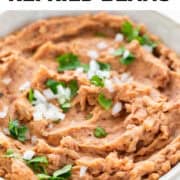 Vegan refried beans in a bowl, garnished with chopped onion and parsley.