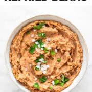 Bowl of vegan refried beans topped with chopped onion and fresh parsley.