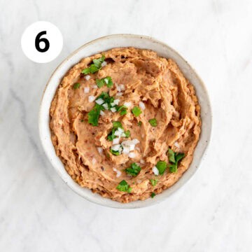 Finished vegan refried beans in a bowl, garnished with fresh toppings.